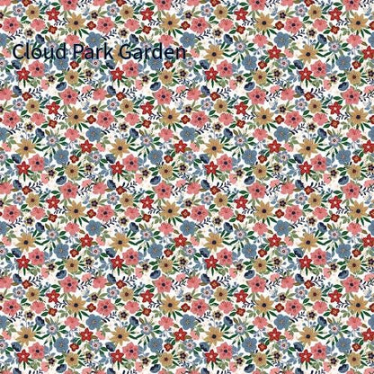 cotton fabric collection spoonful of sugar this one is a repeating pattern of small flowers in shades of blue, gold, white, and green on a white background called "Cloud Park Garden" The floral design is dense and covers the entire surface.
